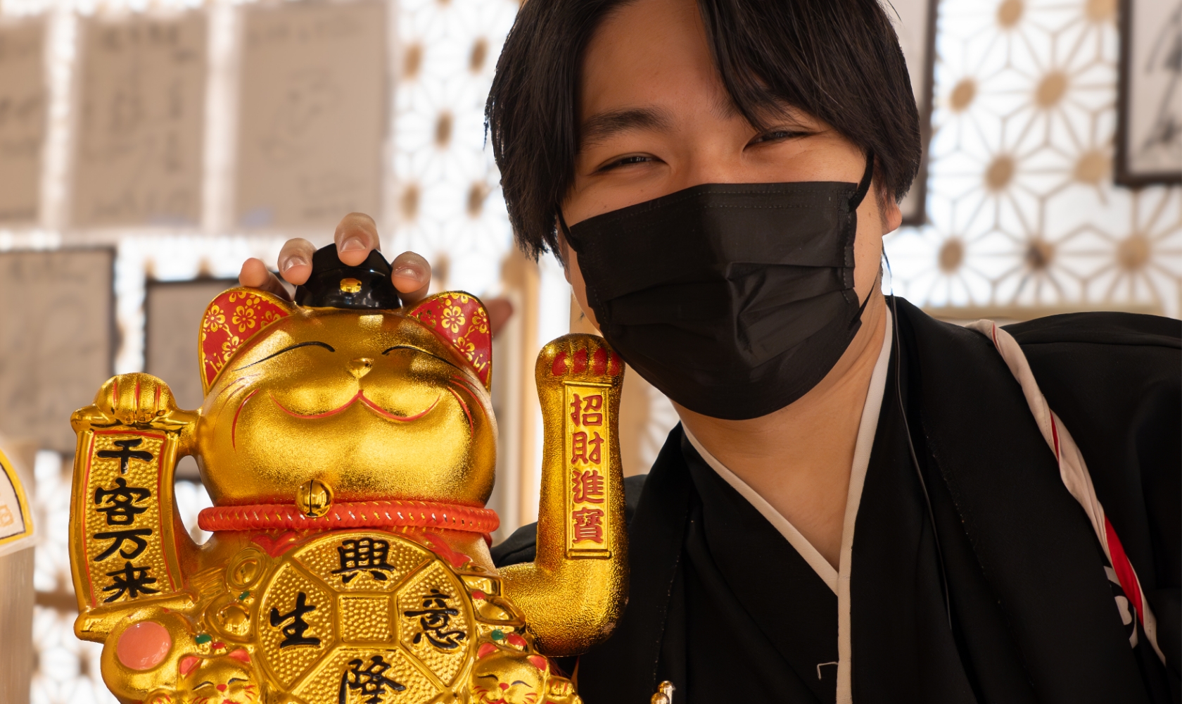 招き猫の隣で笑顔の和装男性スタッフ