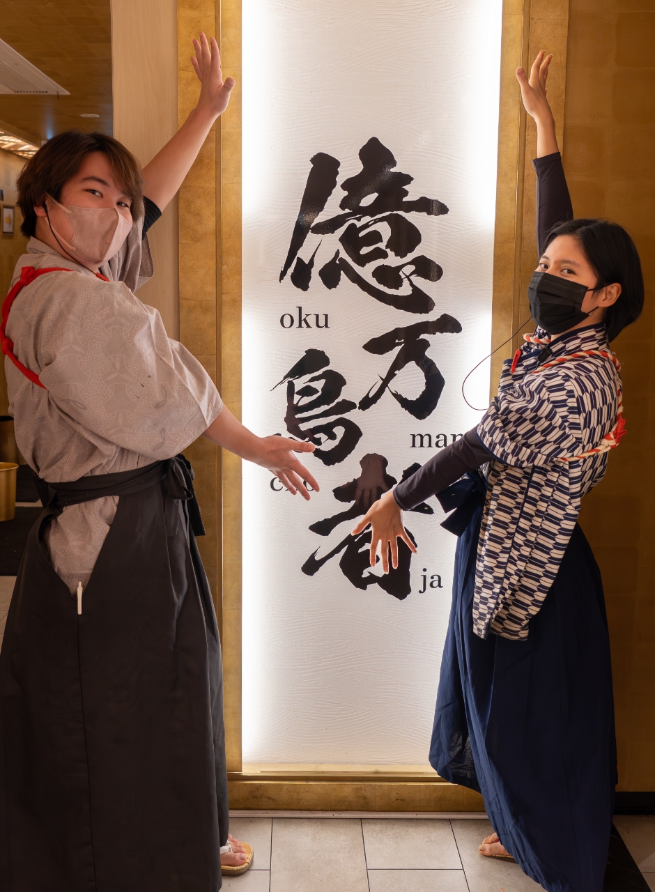 億万鳥者看板前のスタッフ2人